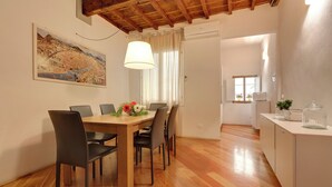 A dining area with a wooden table and chairs, a painting on the wall, and a kitchen in the background. - Mamo Florence - San Lorenzo Apartment (Florence)