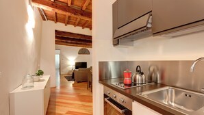 A modern kitchen with stainless steel appliances, wooden flooring, and a dining area in the background. - Mamo Florence - San Lorenzo Apartment (Florence)