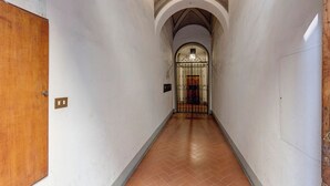 A hallway with a wooden door on the left, a tiled floor, and a metal gate at the end.