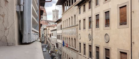 A narrow street with buildings on either side, featuring arched windows and a mix of architectural styles.