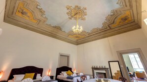 A hotel room with two beds, ornate ceiling, chandelier, and a fireplace. - Mamo Florence - Tintori Luxury Palace (Florence)