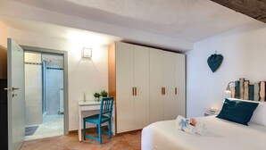 A bedroom with a bed, a desk with a chair, a wardrobe, and a bathroom visible through an open door. - Mamo Florence - Toscanella Apartment (Florence)