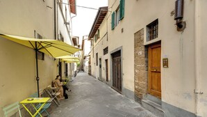 A narrow street with outdoor seating under yellow umbrellas, stone buildings, and a wooden door. - Mamo Florence - Toscanella Apartment (Florence)
