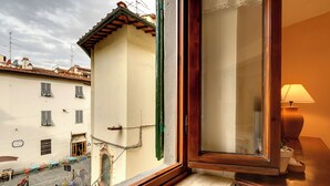 A window with a view of a street, a building with a tiled roof, and a lamp on a table. - Mamo Florence - Toscanella Apartment (Florence)
