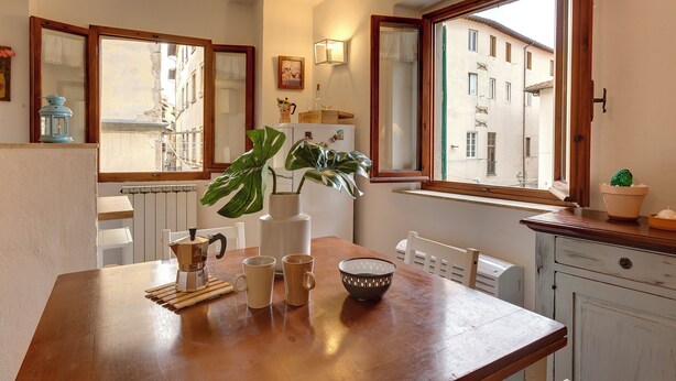 A dining area with a wooden table, two chairs, a coffee maker, and a potted plant. - Mamo Florence - Toscanella Apartment (Florence)