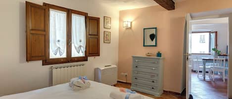A bedroom with a bed, a radiator, a dresser, and a door leading to a dining area.