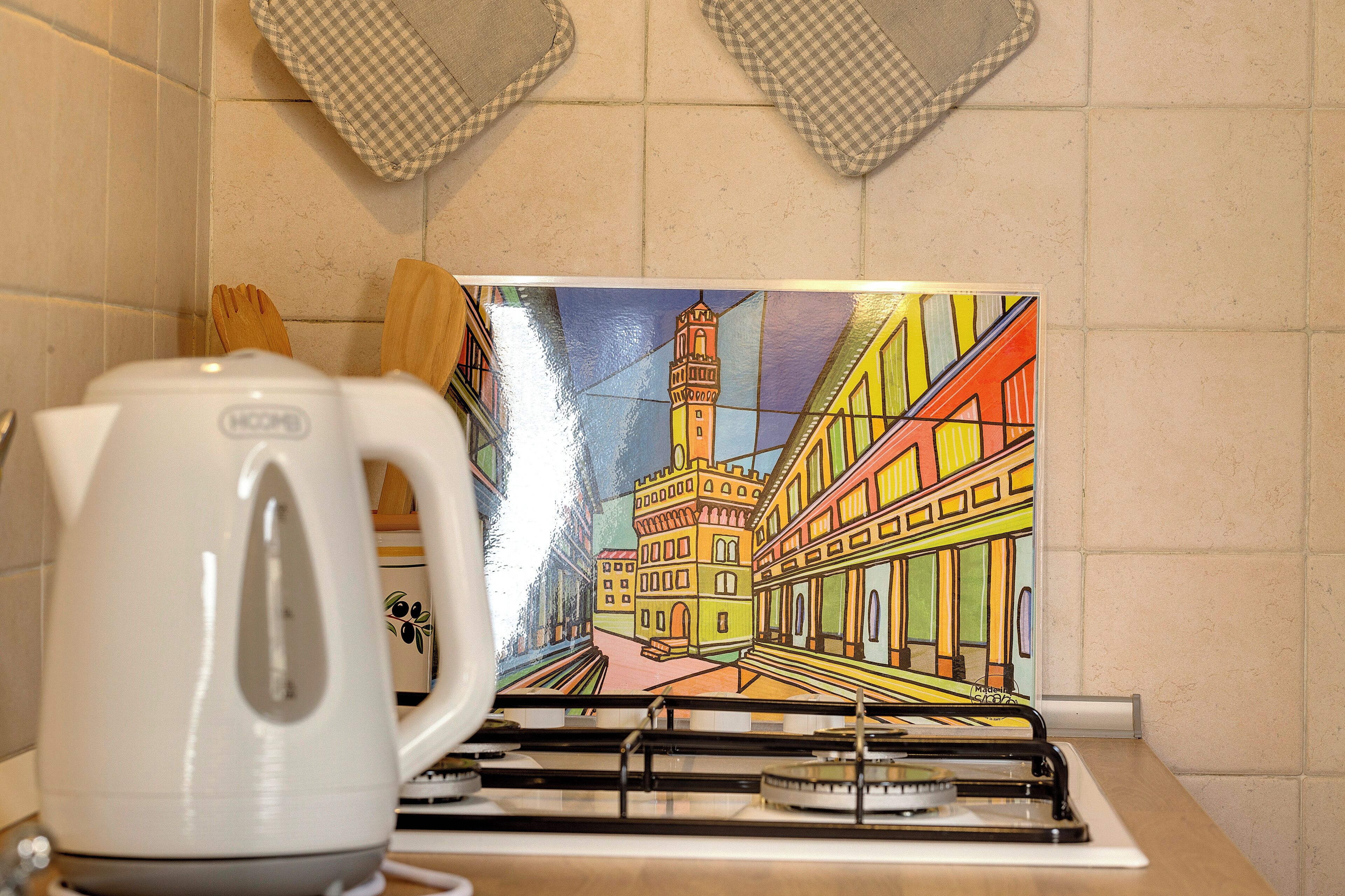 Una cucina con un quadro colorato di un paesaggio urbano, un bollitore e utensili di legno sul piano di lavoro.