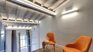Una habitación moderna con piso de madera, techo blanco con vigas a la vista y una silla de color naranja brillante.