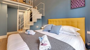 Una habitación de hotel con una cama, un cabecero amarillo, una escalera y obras de arte en la pared.