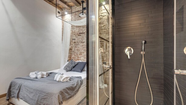 A modern bedroom with a bed, a glass shower enclosure, and exposed brick walls. - Mamo Florence - Vigna Vecchia Studio (Florence)