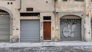 A building facade with closed metal shutters, a wooden door, and graffiti on one shutter. - Mamo Florence - Vigna Vecchia Studio (Florence)