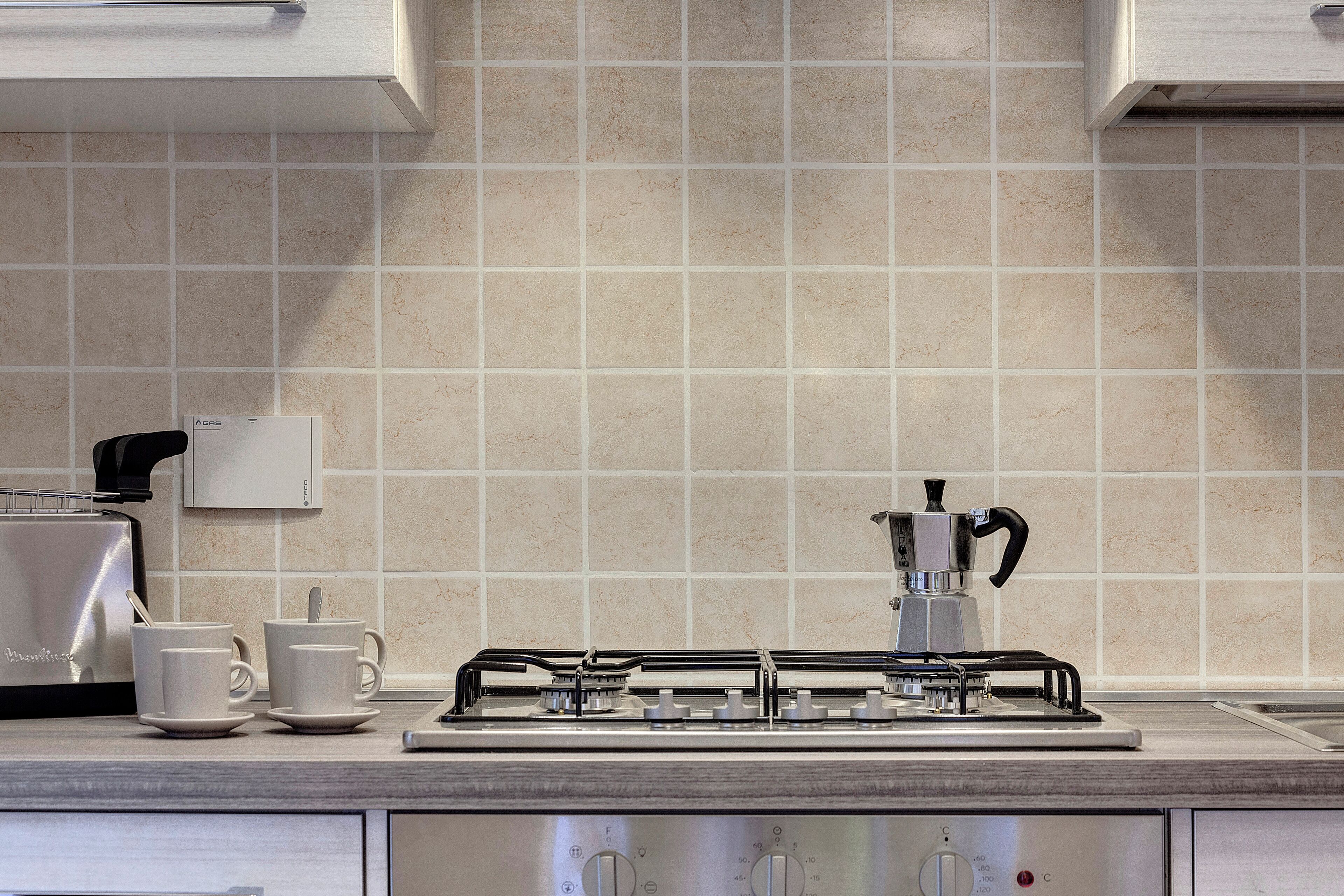 A modern kitchen with a gas stove, two white cups, and a coffee maker.