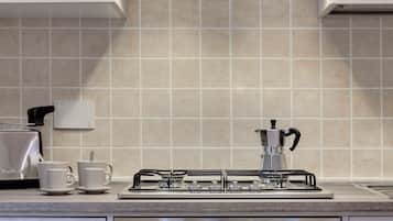 A modern kitchen with a gas stove, two white cups, and a coffee maker.