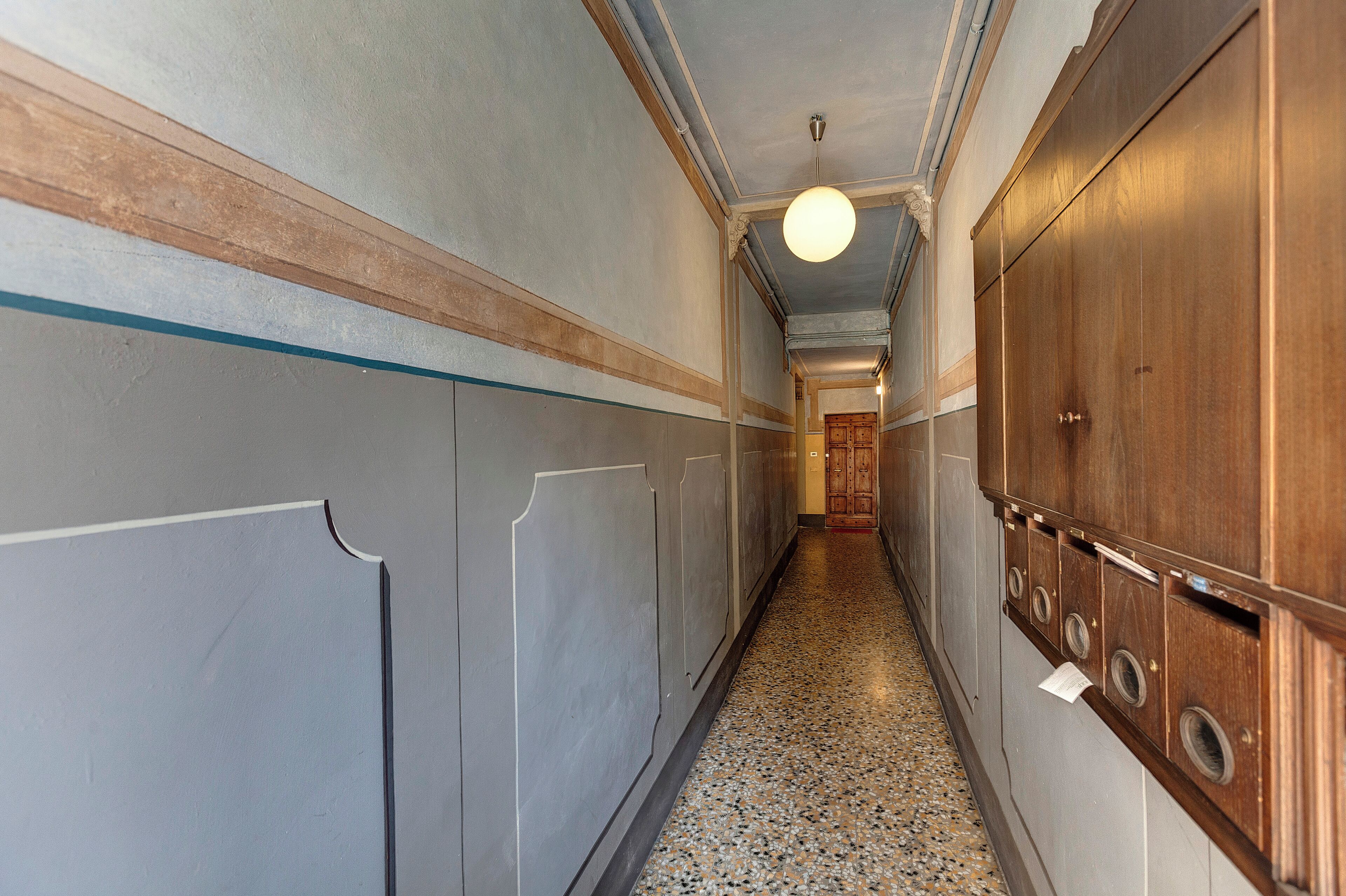 A hallway with a polished stone floor, wooden lockers, and a light fixture on the ceiling.