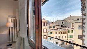 A room with a window overlooking a cityscape, a radiator, and a chair. - Mamo Florence - Zante Aparment (Florence)
