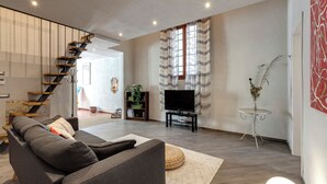 Un salon moderne avec un canapé gris, un téléviseur et un escalier.