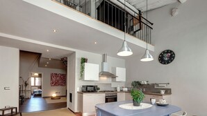 Une cuisine spacieuse équipée d’appareils modernes, un coin repas avec une table bleue et un escalier apparent menant à l’étage supérieur.