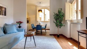 Una sala de estar con sofá, una mesa de comedor con sillas, una planta en maceta y un radiador.