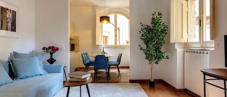 A living room with a sofa, a dining table with chairs, a potted plant, and a radiator.