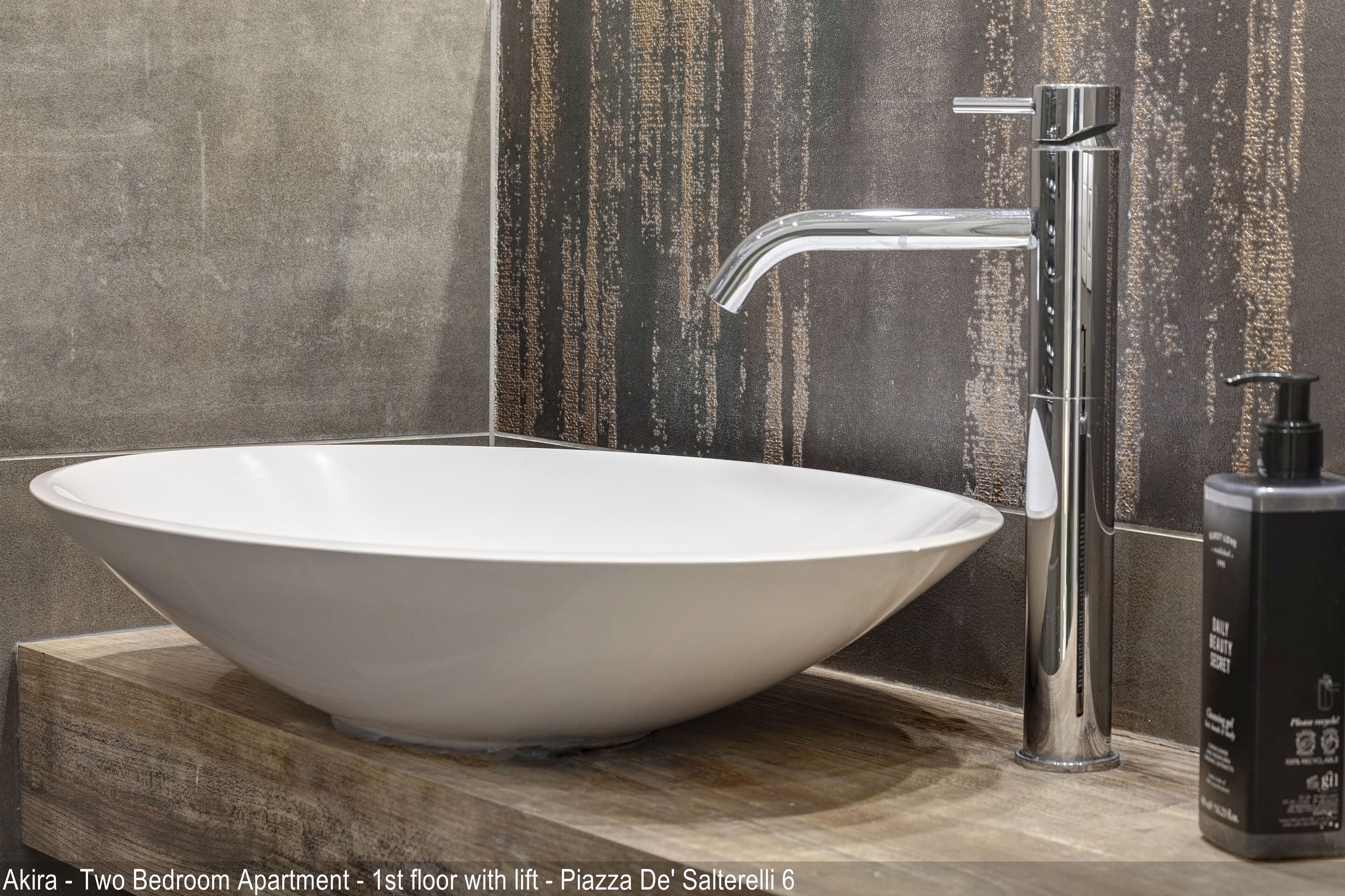 A modern bathroom with a white vessel sink, a chrome faucet, and a soap dispenser on a wooden vanity.