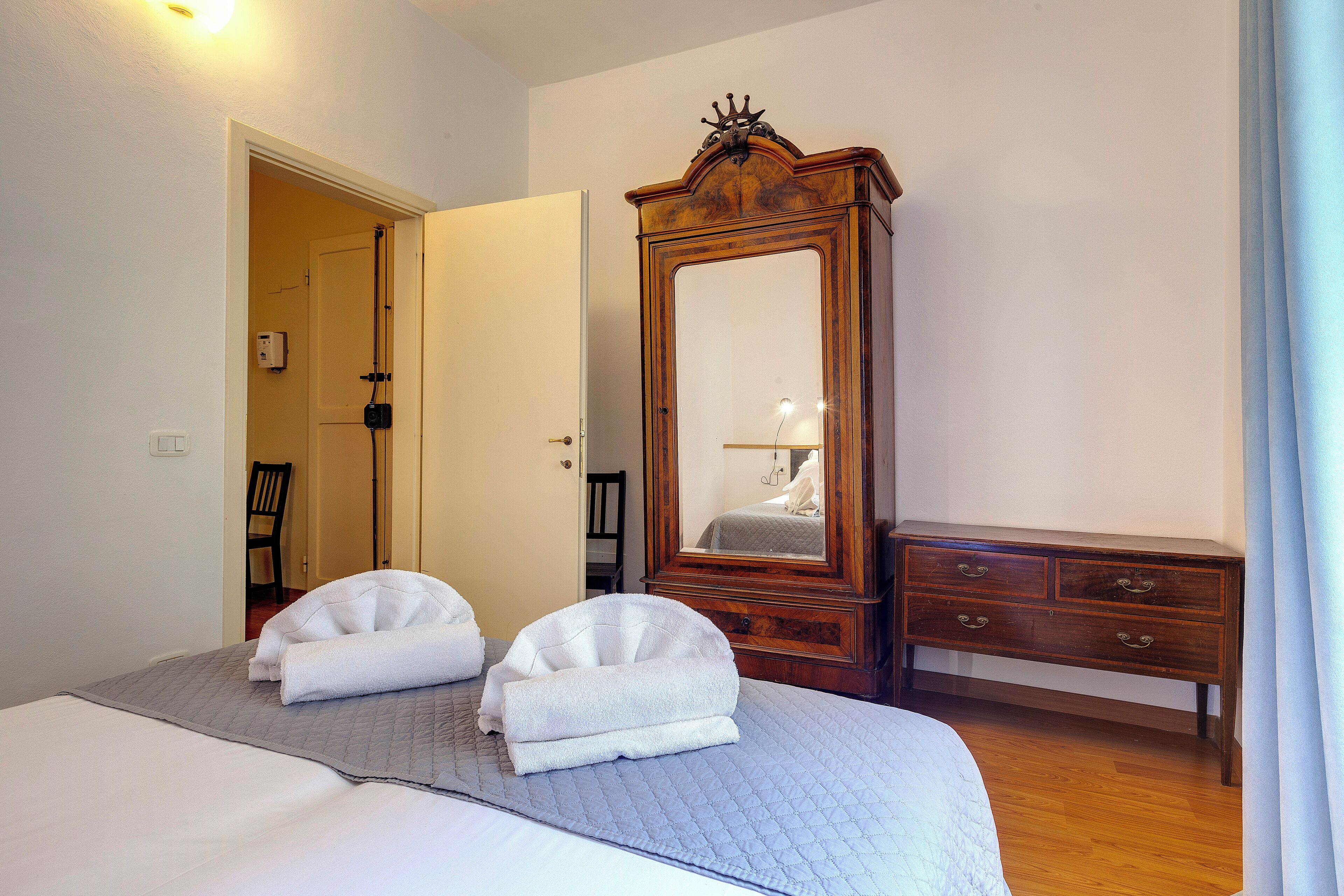 A bedroom with a bed, a wooden dresser, and a large mirror.