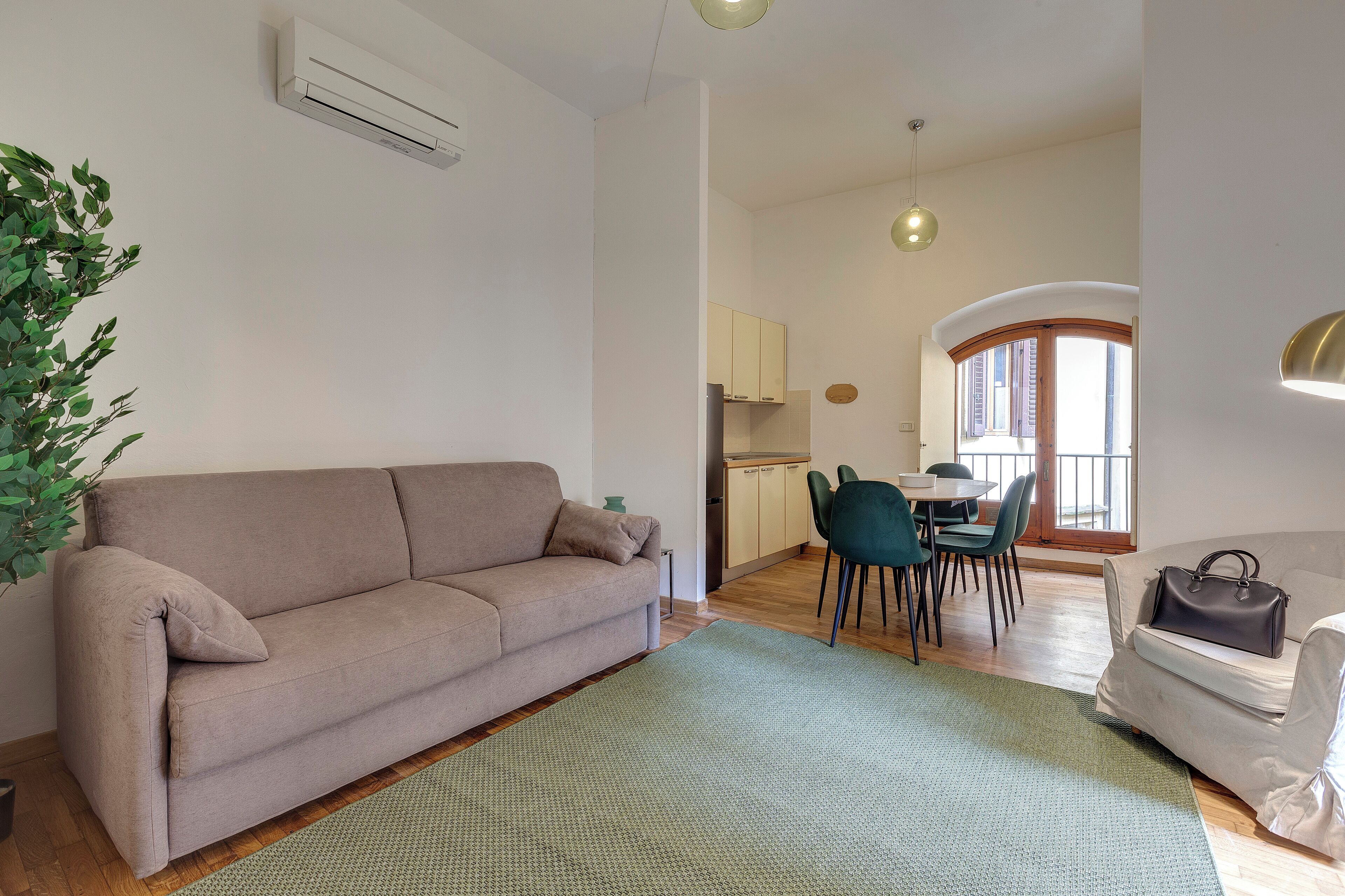 A living room with a sofa, a dining area with chairs and a table, and a kitchen in the background.