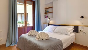 Una cama bien hecha con dos toallas, una mesita de noche con lámpara y una ventana con cortinas.