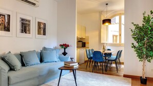Una sala de estar con sofá, una mesa de centro y un comedor con sillas y una mesa. Hay una planta en maceta y cuadros en la pared.
