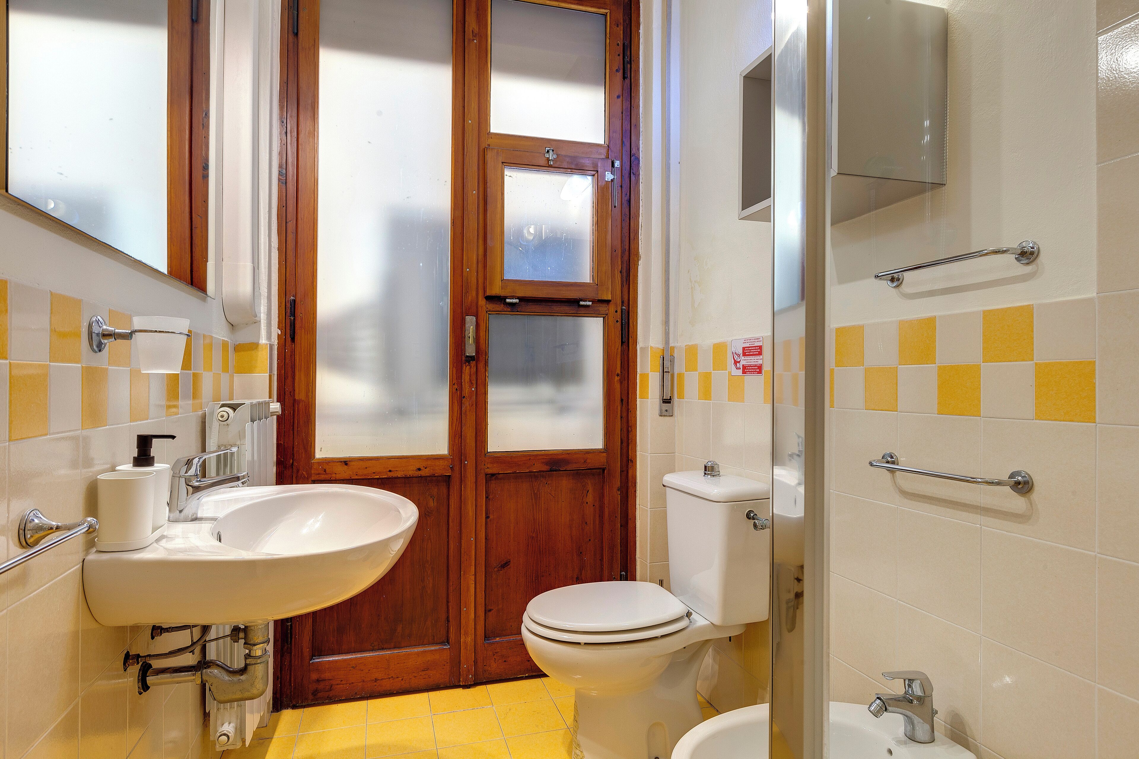 A bathroom with a wooden door, a white sink, a toilet, and a shower area.