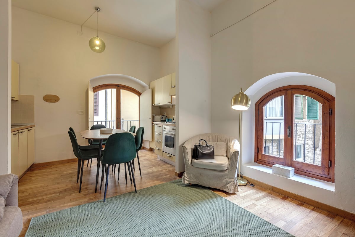 A spacious living area with a dining table, chairs, a sofa, and a window with a view.