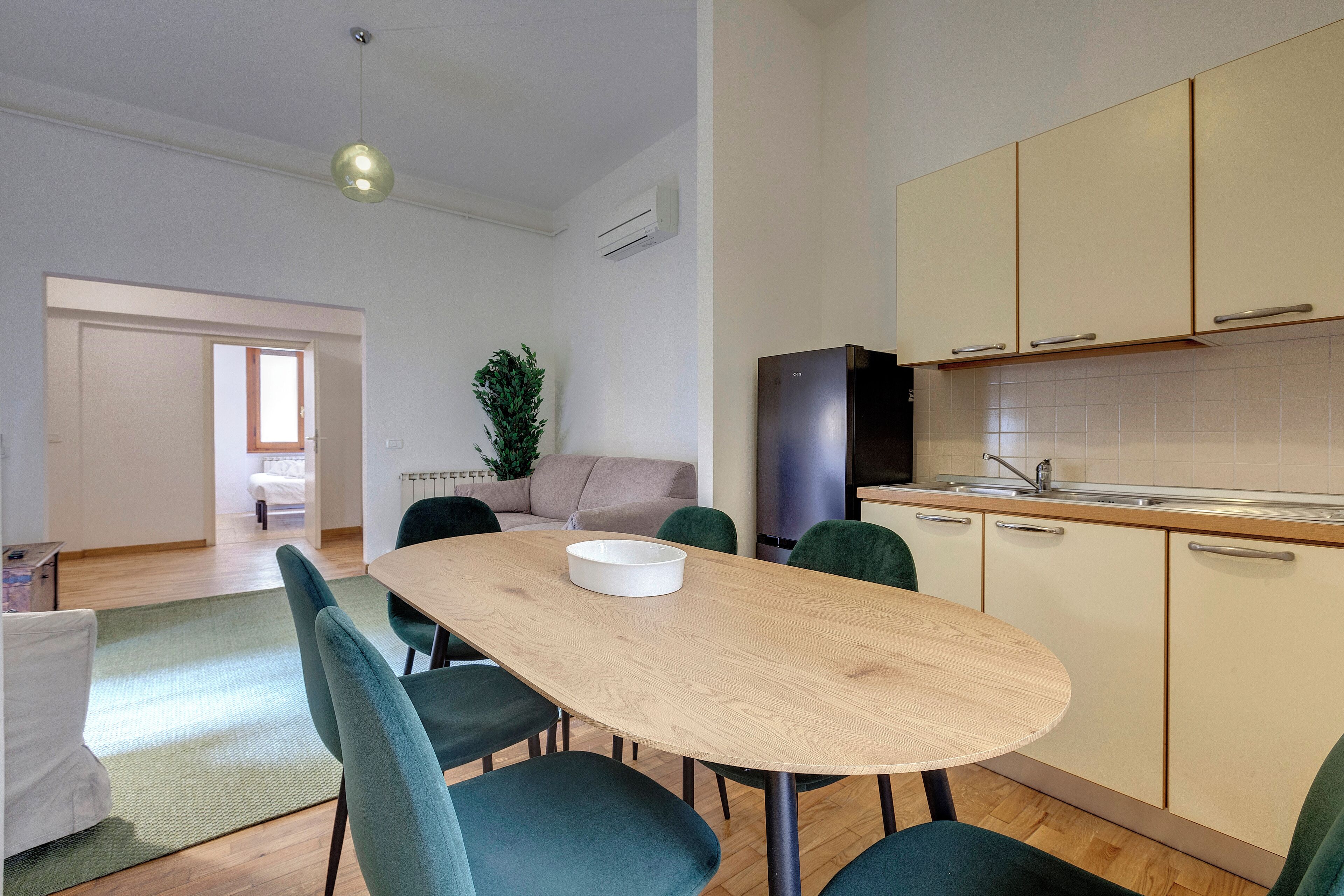 A modern kitchen with a dining area, featuring a wooden table, green chairs, and a built-in oven.
