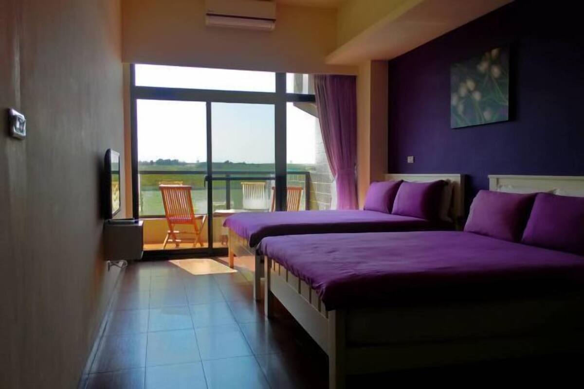 A hotel room with two beds, a balcony with a chair, and a large window offering a view.