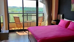 A bedroom with a large bed, a balcony with chairs, and a view of the countryside. - Rainbowsea Hostel (Penghu)
