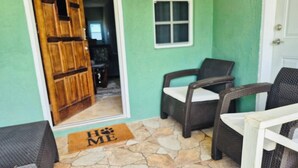 A room with a stone-tiled floor, a wooden door, two wicker chairs, and a white door frame. - 3-bedroom house in brilliant Potters Village with AC (Potters Village)