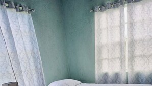 A small, simple room with a bed, a nightstand, and a patterned rug. - 3-bedroom house in brilliant Potters Village with AC (Potters Village)