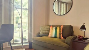 A modern living room with a sofa, a chair, a round mirror, a lamp, and a small table with a toy bus. - Notting Hill - The One One One! -1- (London)