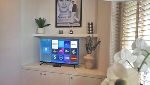 A television on a cabinet with a Netflix logo, surrounded by decorative items and a window with blinds. - Notting Hill - The One One One! -1- (London)