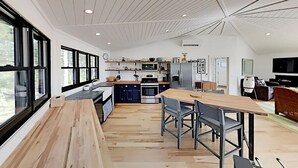 Eine moderne Küche mit Esstisch und Stühlen aus Holz, integrierten Geräten und großen Fenstern.