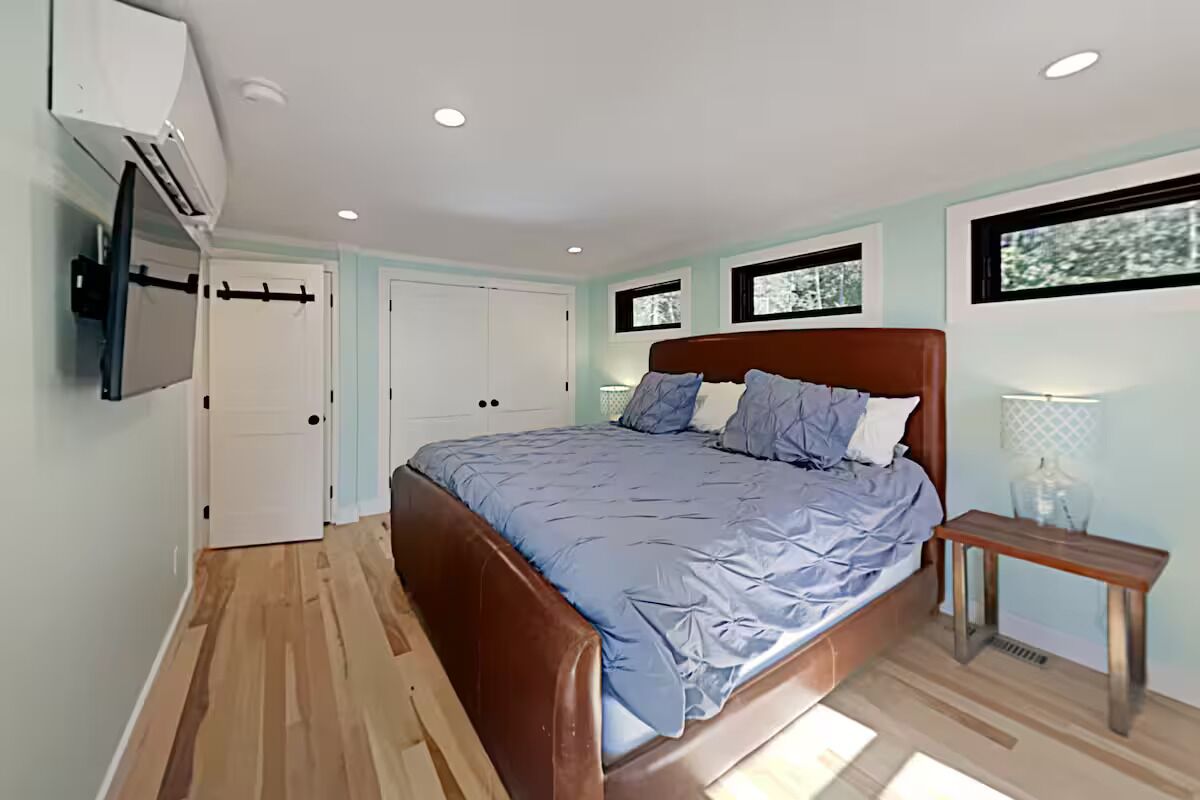 A bedroom with a bed, a bedside table, a wall-mounted TV, and a window.