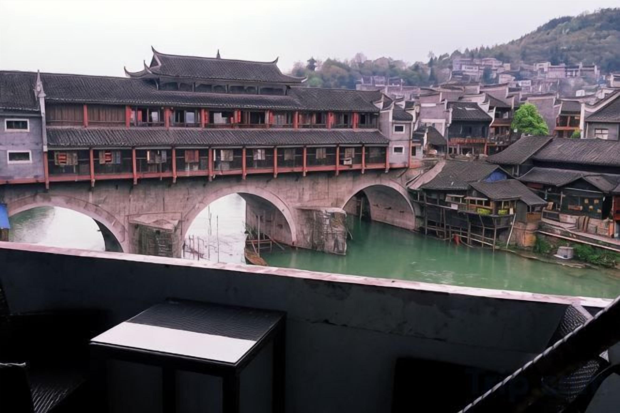 A traditional Chinese architectural style building with a bridge over a water body, likely a river, with multiple arches.