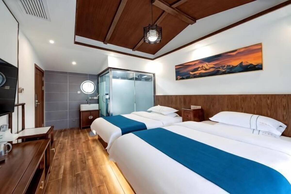A hotel room with two beds, a wooden ceiling, a painting, a mirror, and a desk.