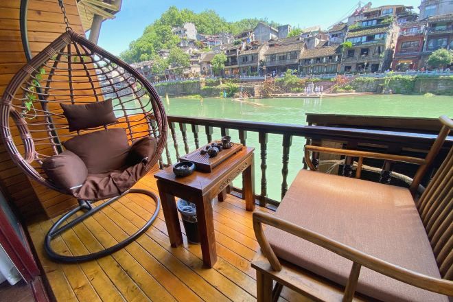 A wooden deck with a hanging chair and a cushioned bench, overlooking a river with buildings in the background.
