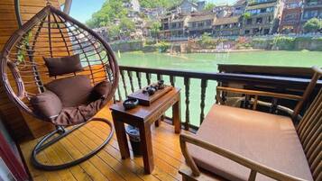 A wooden deck with a hanging chair and a cushioned bench, overlooking a river with buildings in the background.