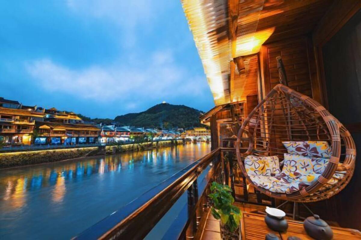 A riverside view with traditional buildings, a wooden balcony, and a wicker chair.