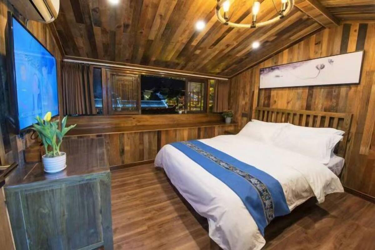 A wooden-paneled room with a bed, a television, and a window with a view.