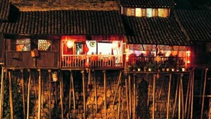 A traditional building with a stone base and tiled roof, featuring a balcony with railings and potted plants. - yun shui jian jiangjing minsu (Fenghuang County)