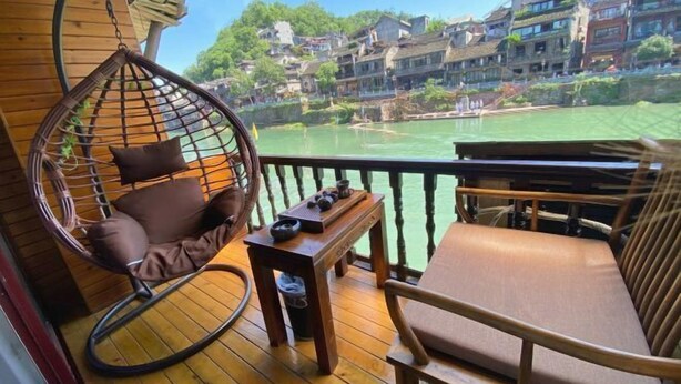A wooden deck with a hanging chair and a cushioned bench, overlooking a river and traditional buildings. - yun shui jian jiangjing minsu (Fenghuang County)