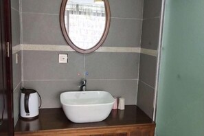 Un baño con un lavamanos blanco, un espejo redondo y una tetera en la encimera.