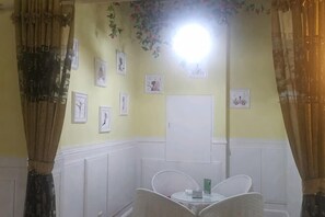 A room with a white cabinet, a chair, a small table with a green object, and framed pictures on the wall.