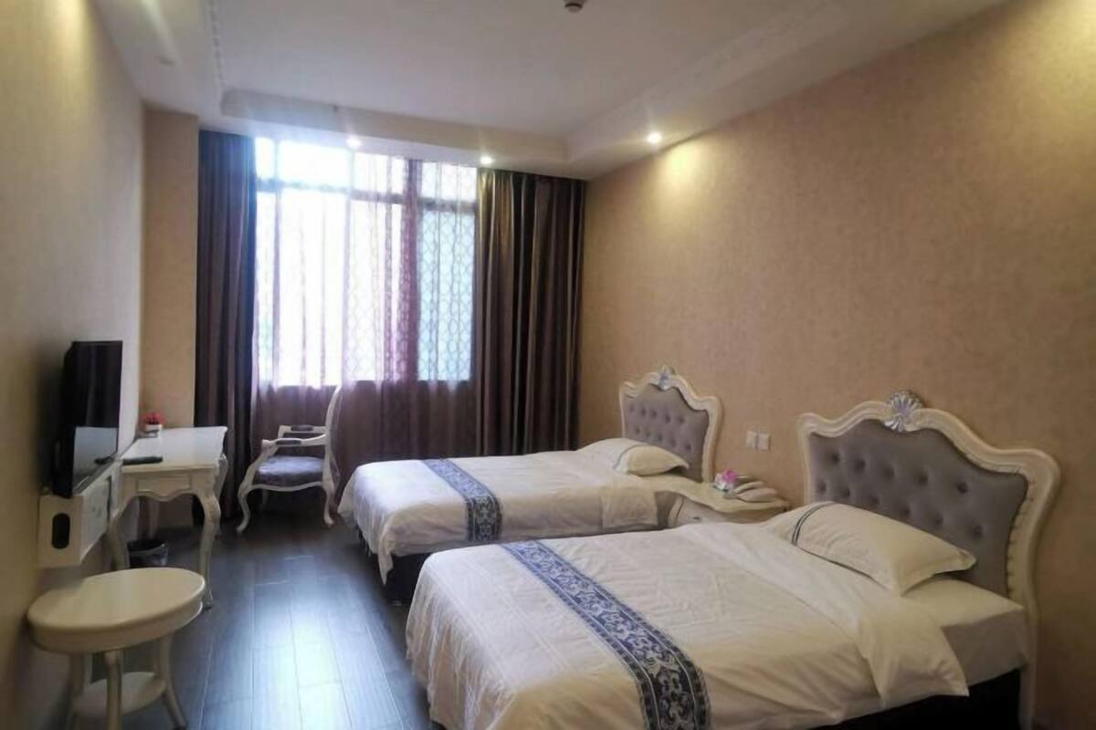 A hotel room with two beds, a desk, a chair, and a television.